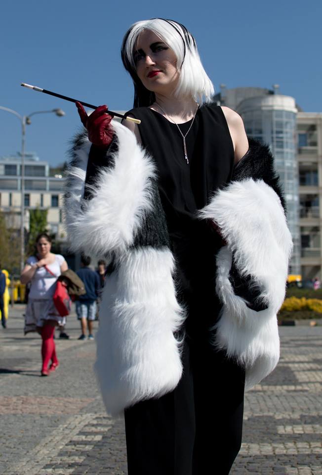 akela dressed a cruella de vil from once upon a time in long sleeveless black dress, wig that is half black and half white, red leather gloves, black and white fur coat, dangling silver necklace, sharp eye makeup consisting of black and red lipstick