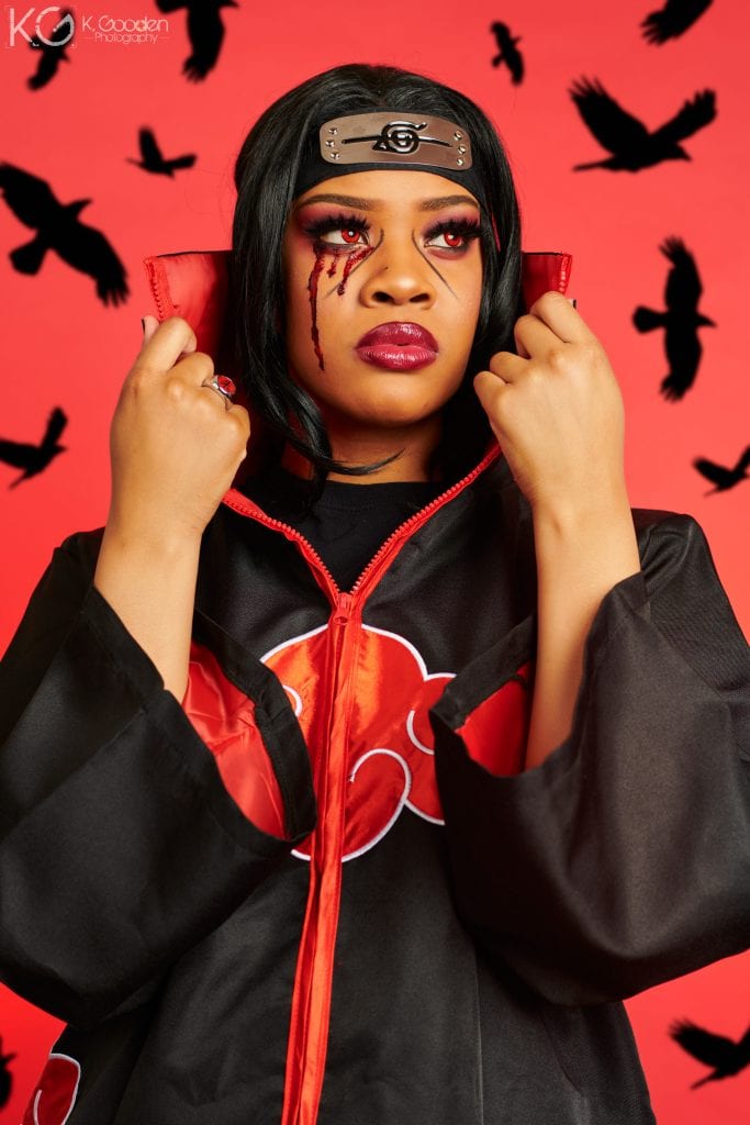 Itachi Uchiha from Naruto. long black satin trench coat zip up with red clouds lined with white embroidery and red lining in jacket. red ring on right hand ring finger, black hair, red contacts, smoky red/black eye shadow, black lines under the eyes out to mid cheeks, fake blood coming from the right eye.