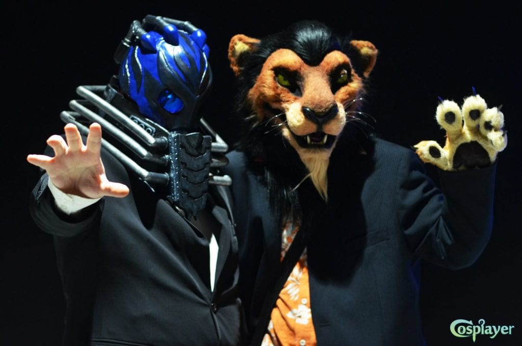 akela and ikasu dressed as all for one from my hero academia with blue helmet, silver chest guard, black suit. akela dressed as scar from the lion king in an ornage patterned shirt and suit jacket.