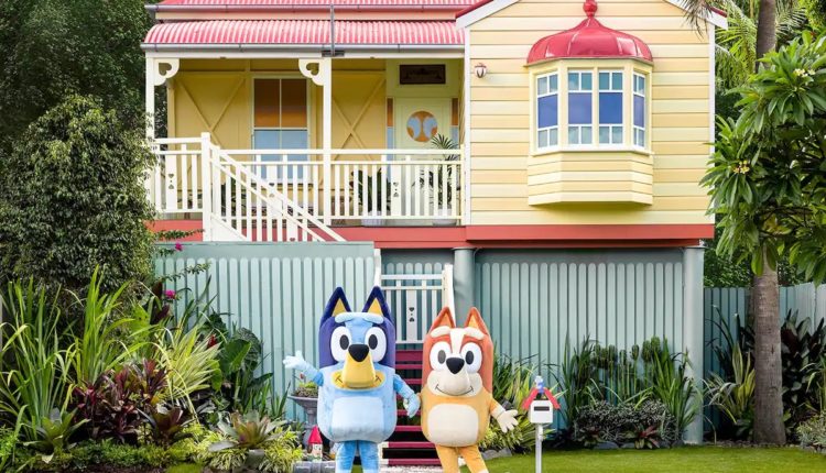 Cartoon characters Bingo and Bluey Heeler standing in front of the Airbnb Bluey house
